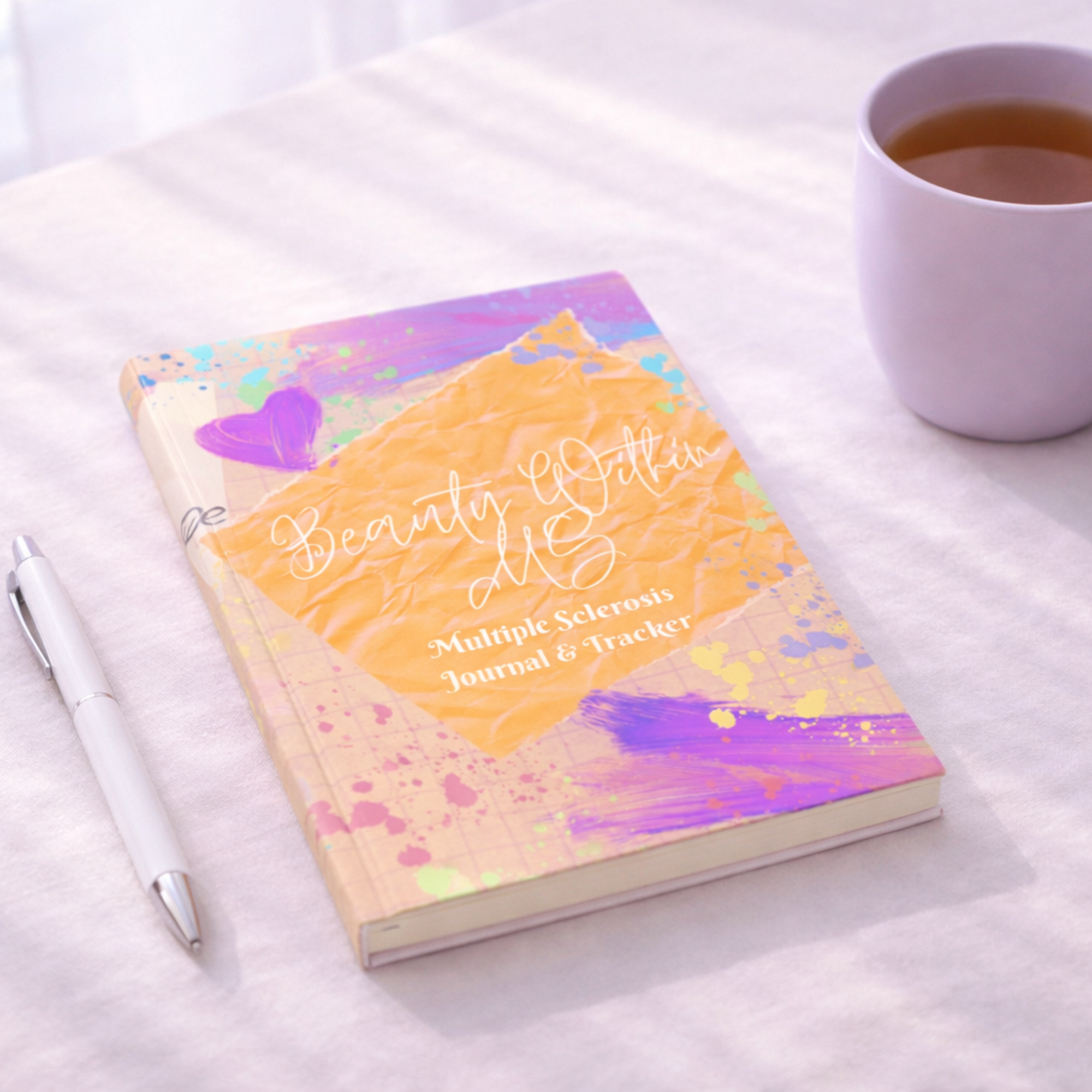 Guided wellness journal for multiple sclerosis resting on a desk with a pen and tea